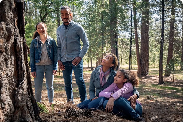 A family of four gather at the base of a tall tree in a forest.