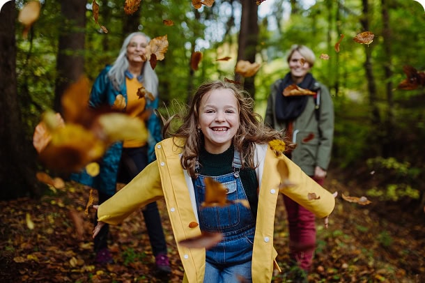 A young laughing as runs ahead of her mother and grandmother through the forest.