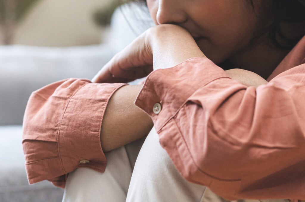 Close-up of a person sitting with knees drawn up, arms wrapped around their legs in a posture of distress.