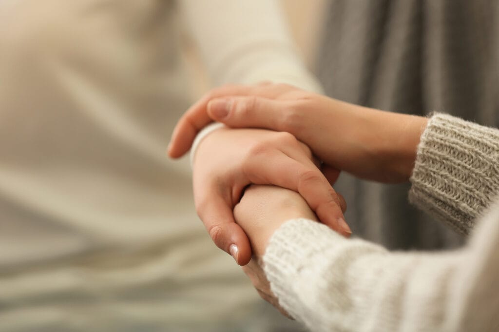 A close-up of one person tenderly holding another's hand, offering comfort.
