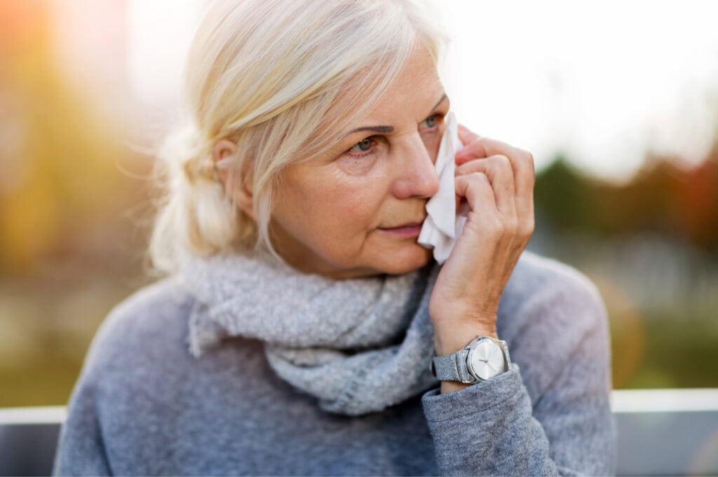 An older woman dabbing her eye with a tissue, visibly emotional.