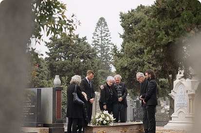 A group of solemn mourners dressed in black gathered around a coffin in a cemetery.