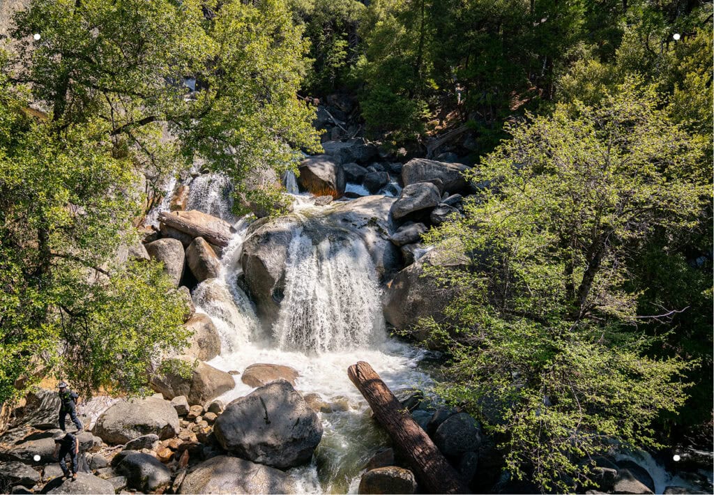 A cascading waterfall tumbles over large boulders through a lush green forest.