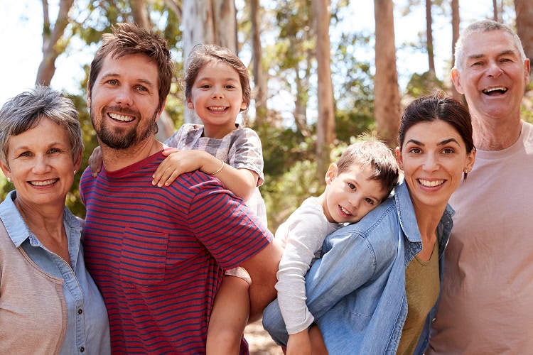 A multigenerational family smiling in a sunlit forest.