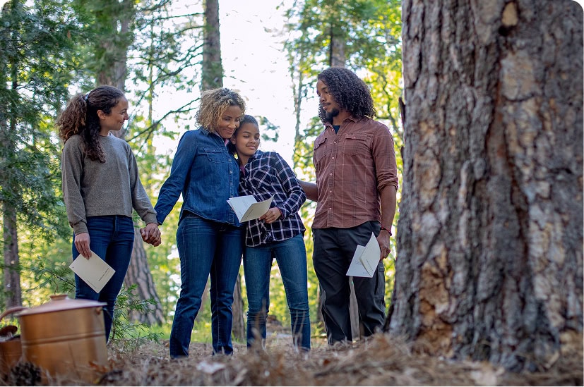 A family of four gathered around a large tree, each holding booklets.