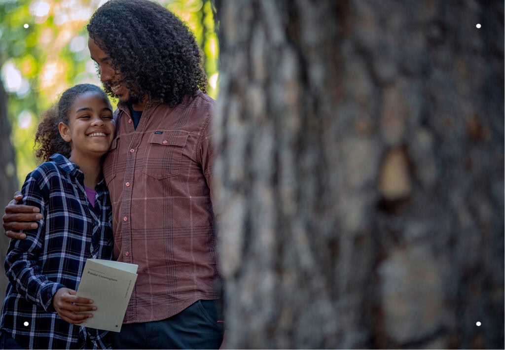 A father lovingly embraces his daughter next to large Memorial Tree.