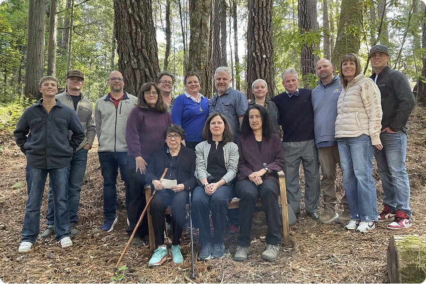 A portrait of multigenerational family gathered in front of a Memorial Tree in the forest.