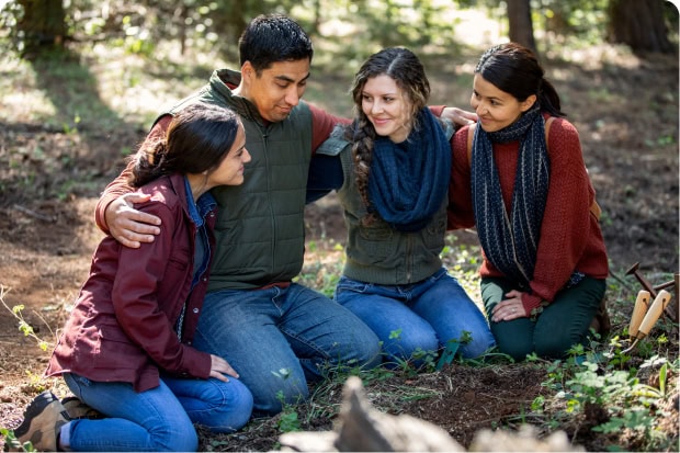 A family of four sit on the forest floor smiling and embracing each other.